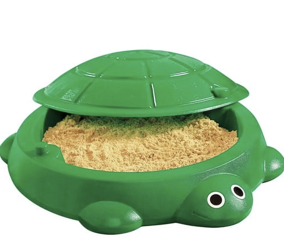 A green turtle-shaped sandbox with an open top, filled with play sand.